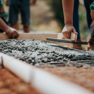 Construction workers leveling fresh cement on a sunny day at an outdoor site.