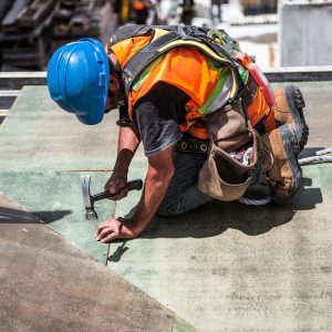 A skilled construction worker in protective gear hammering a rooftop panel.